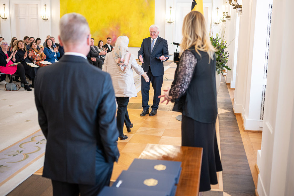 Bundespräsident Frank-Walter Steinmeier empfängt Nejla Coskun zur Verleihung des Bundesverdienstkreuzes, im Vordergrund stehen Mitarbeiter der Ordenskanzlei des Bundespräsidialamtes